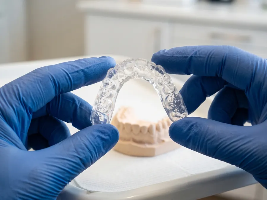A clear custom night guard held in gloved hands over a dental model.